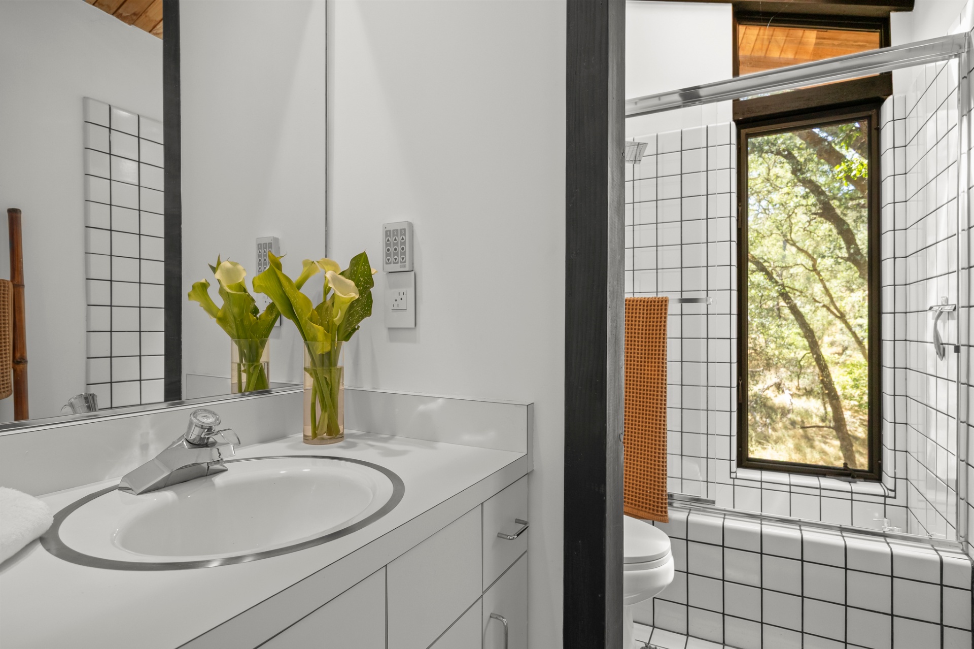 Guest bath with white-tiled tub-shower and forest-view window