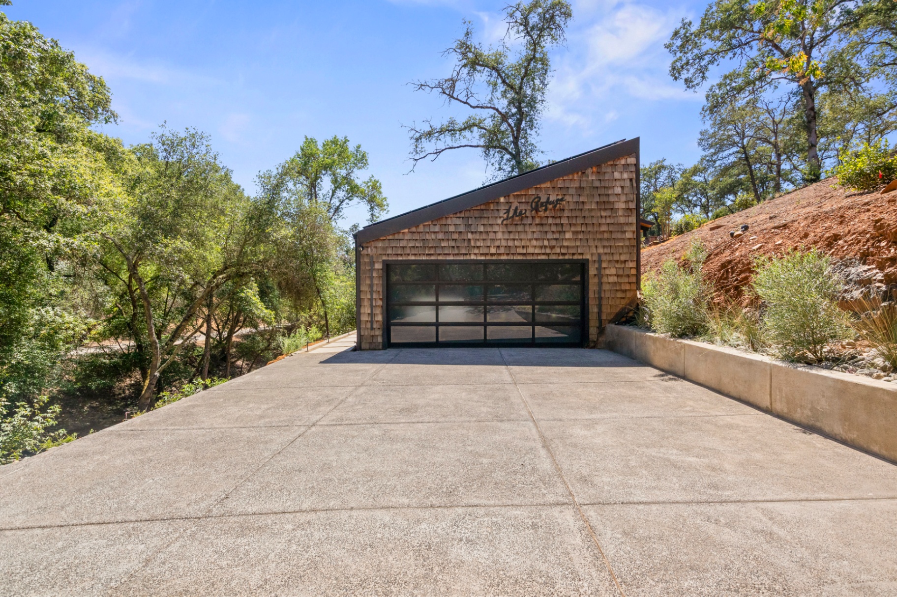 Detached cedar-shingle garage with a glass overhead door at the end of the driveway