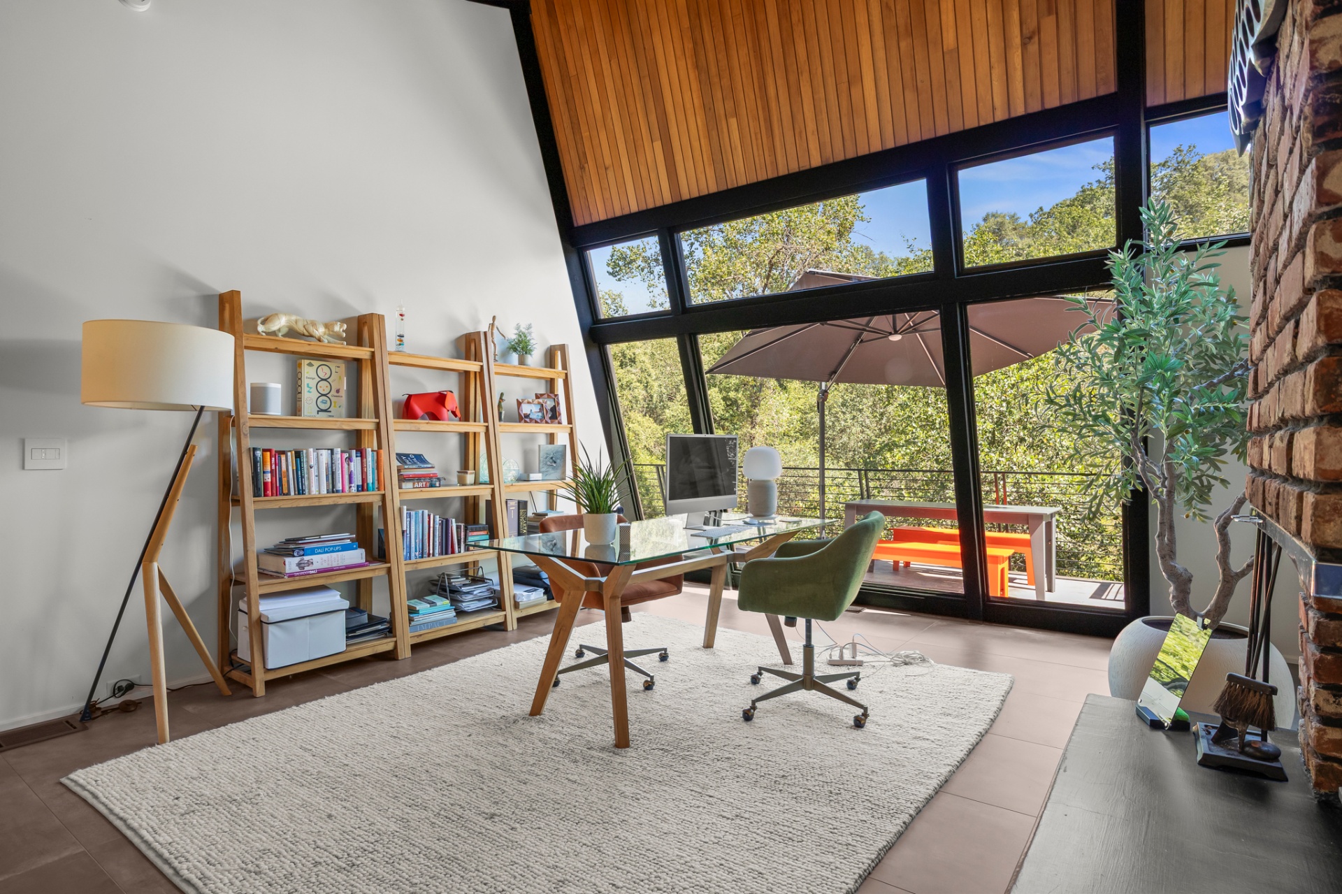 Home office with floor-to-ceiling windows, ladder bookshelves and glass desk