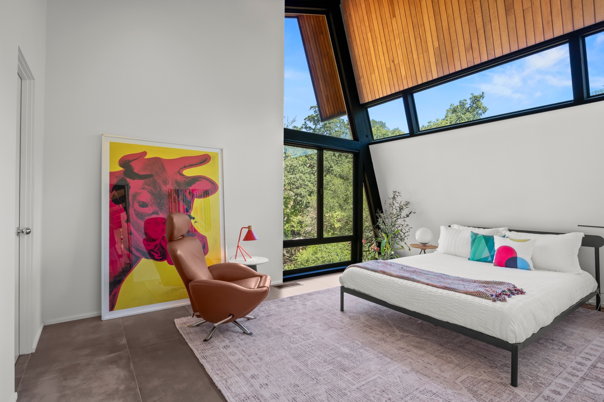 Bright bedroom with a wall of windows, mid-century furniture and pop-art cow poster