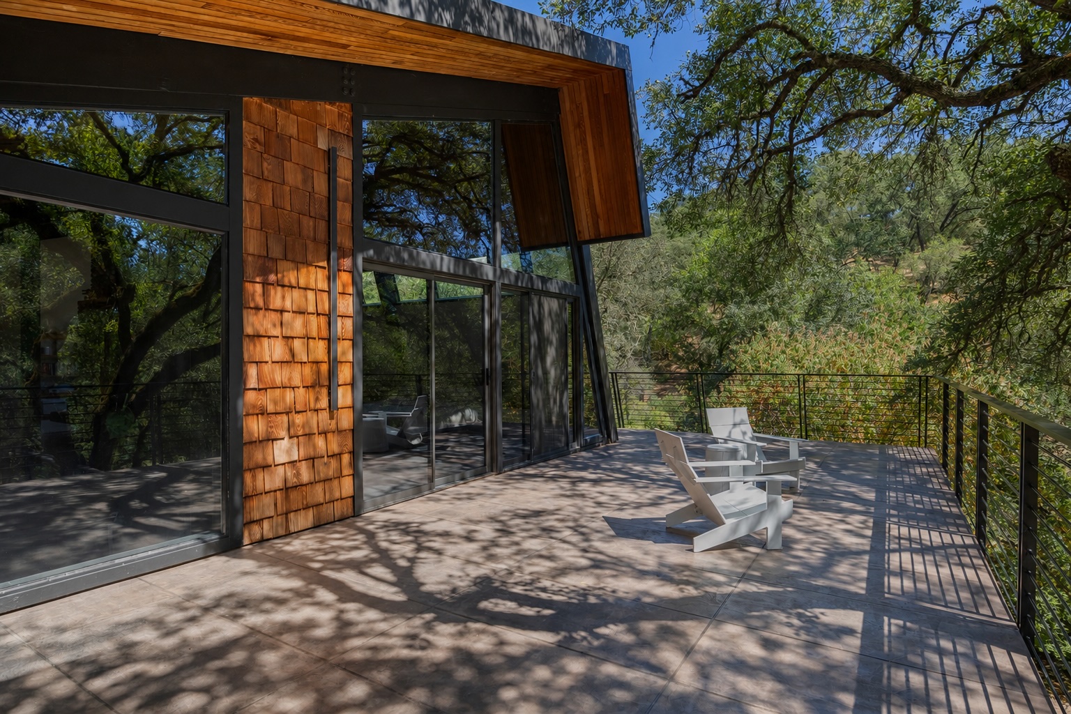 Patio deck with cedar-shingle wall, glass doors and white Adirondack chairs beneath the oak canopy