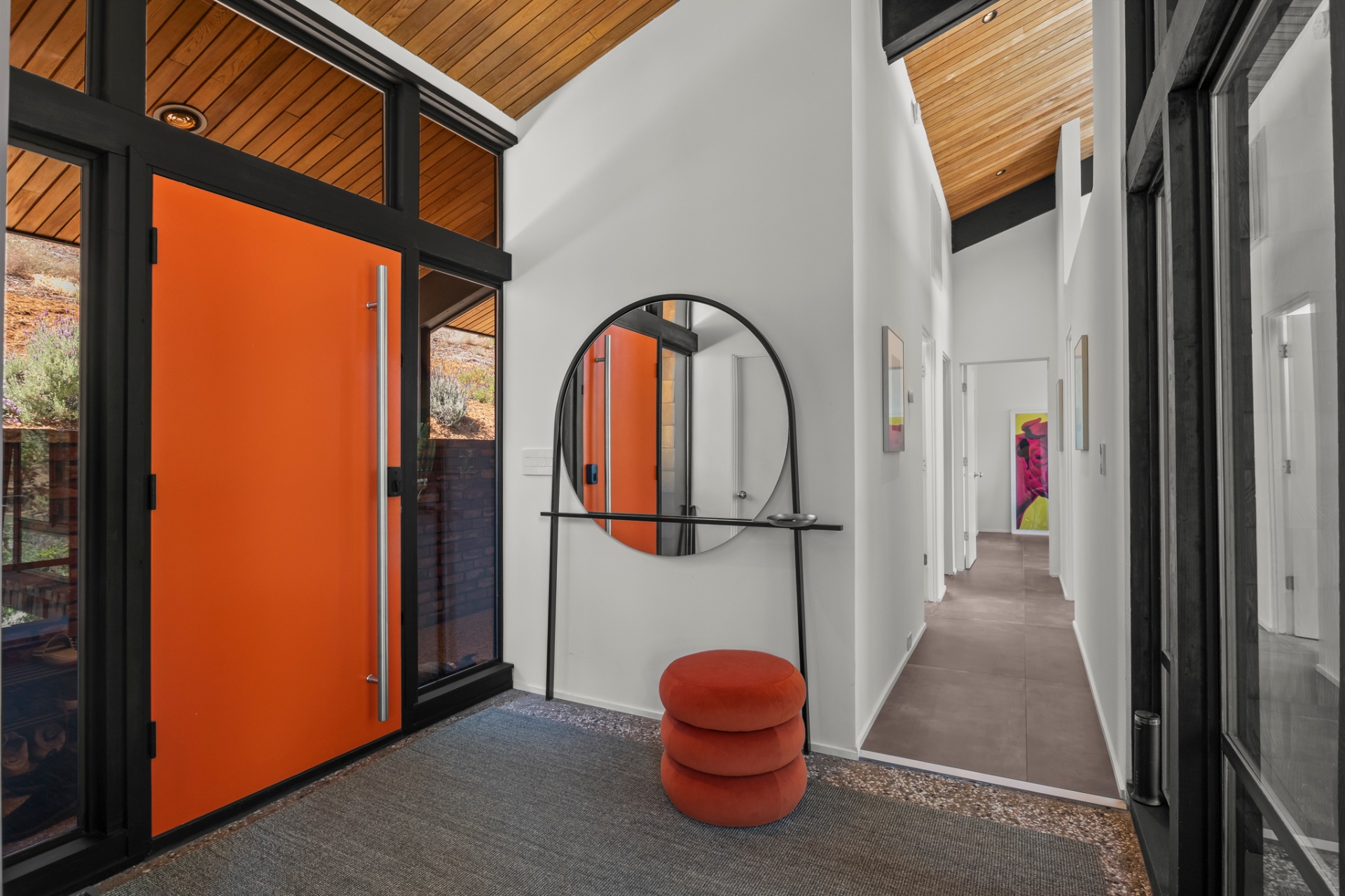 Entry foyer with orange pivot door, round mirror and a long hallway