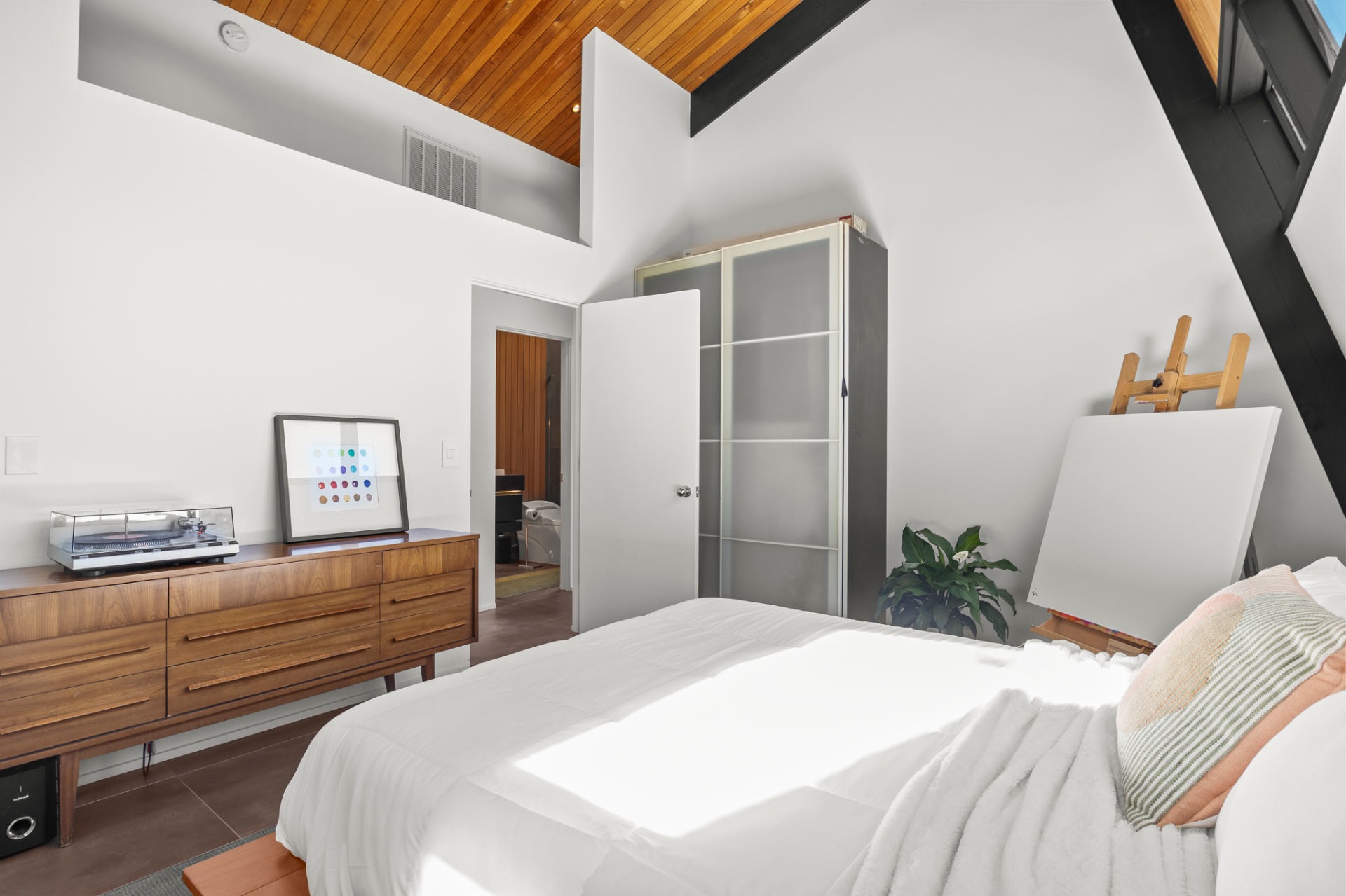 Minimal bedroom with a vaulted ceiling, leather chair and striped art