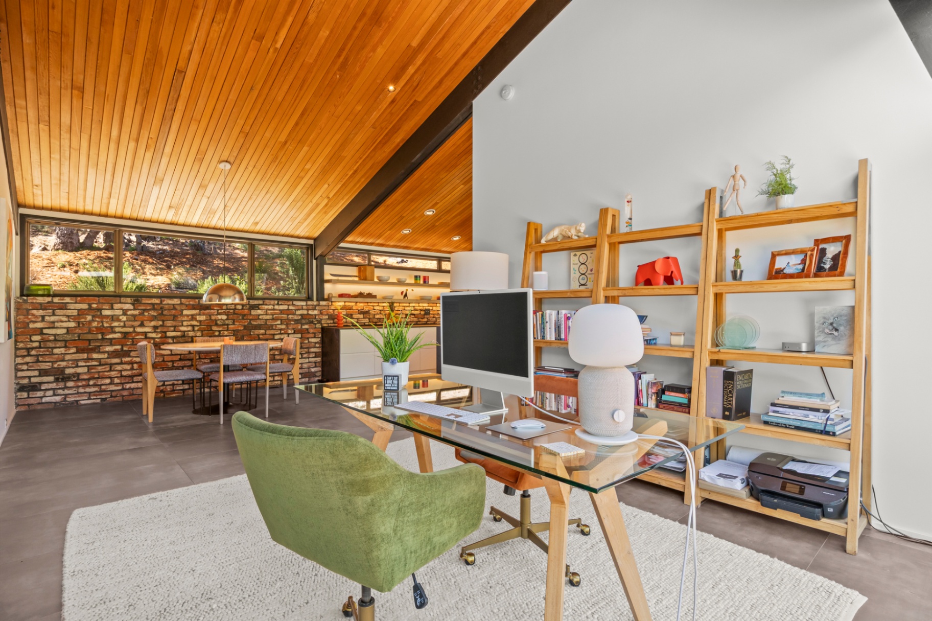 Office with a glass desk, green chair and built-in bookshelves under the wood ceiling