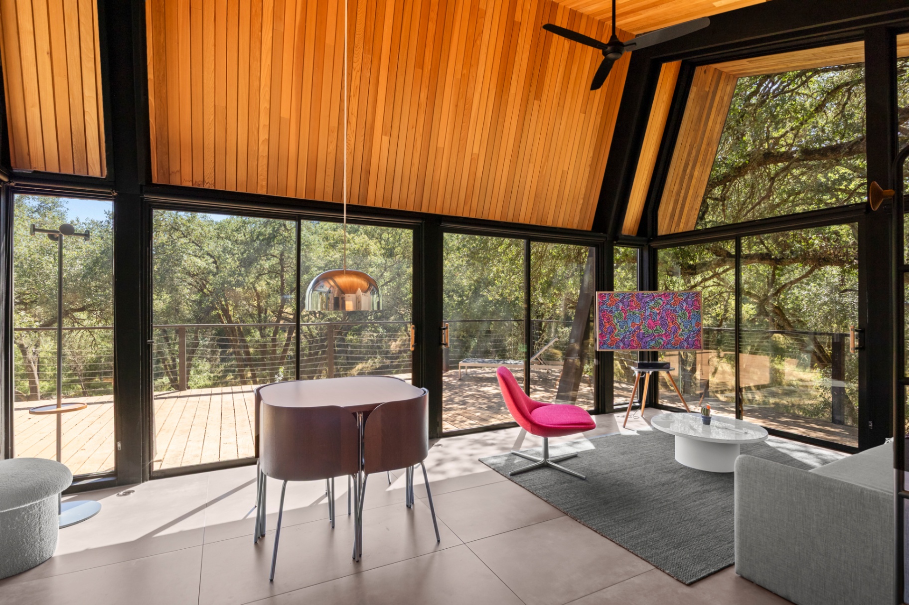 Glass-walled sitting area with round dining table and treetop views