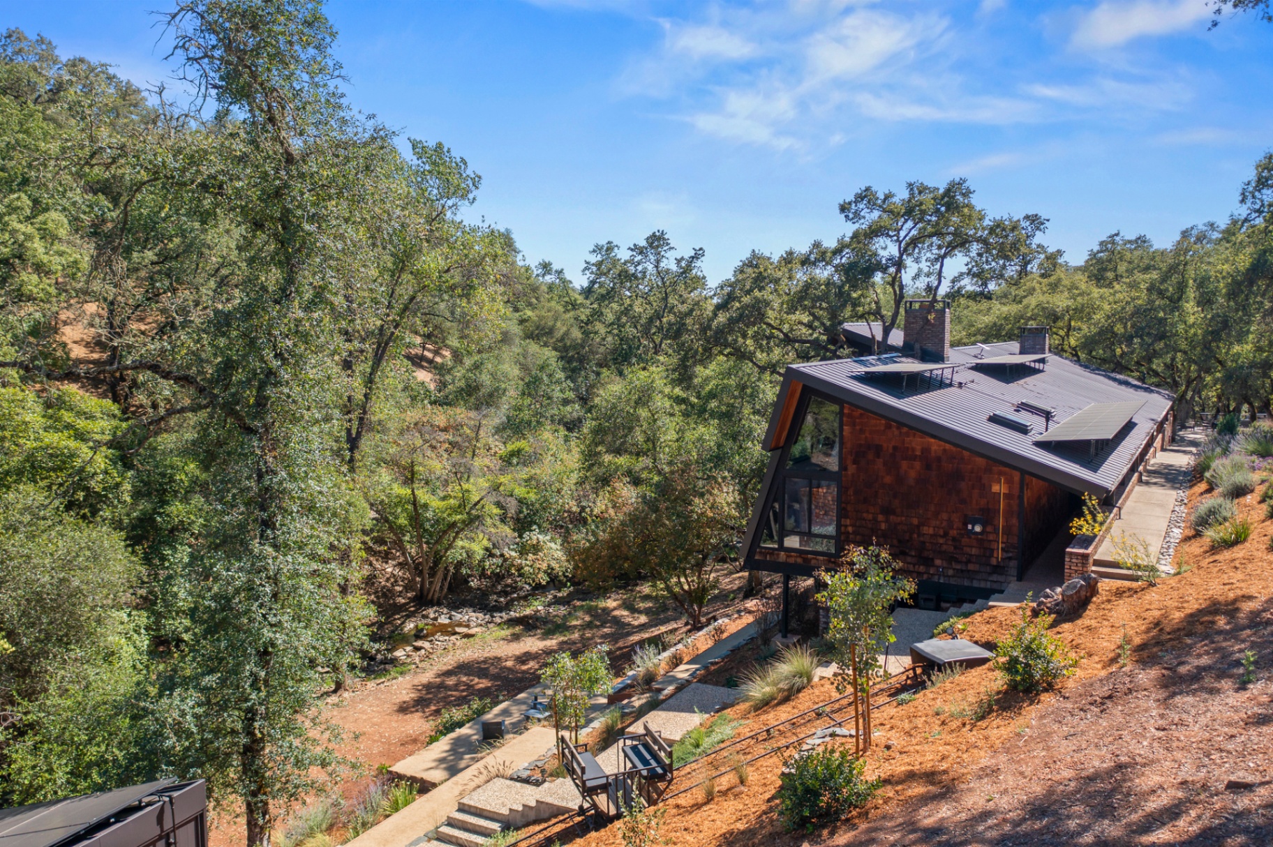 Elevated aerial of the home with a brick chimney and landscaped hillside steps
