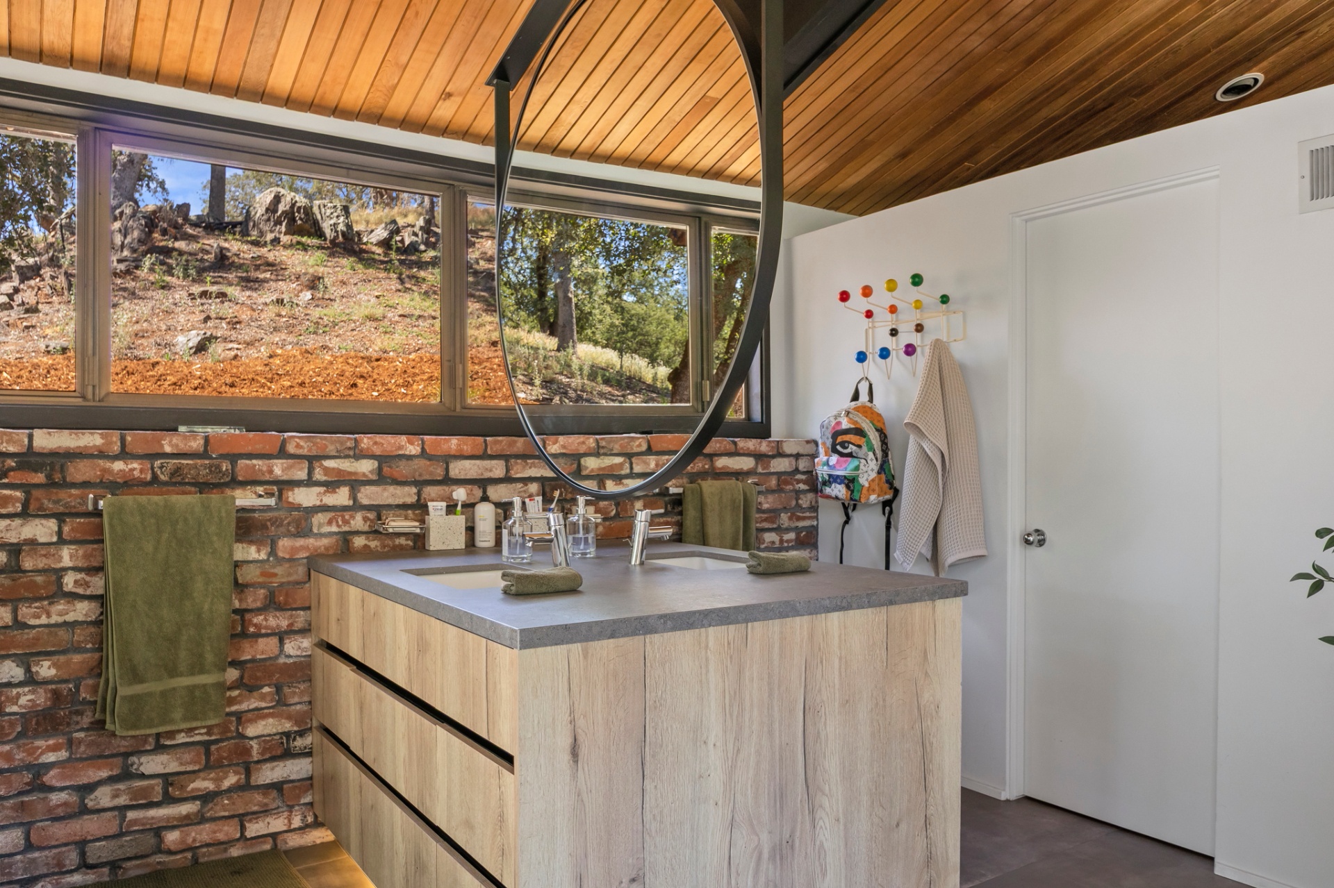 Primary bath with round mirror, wood vanity and hillside window