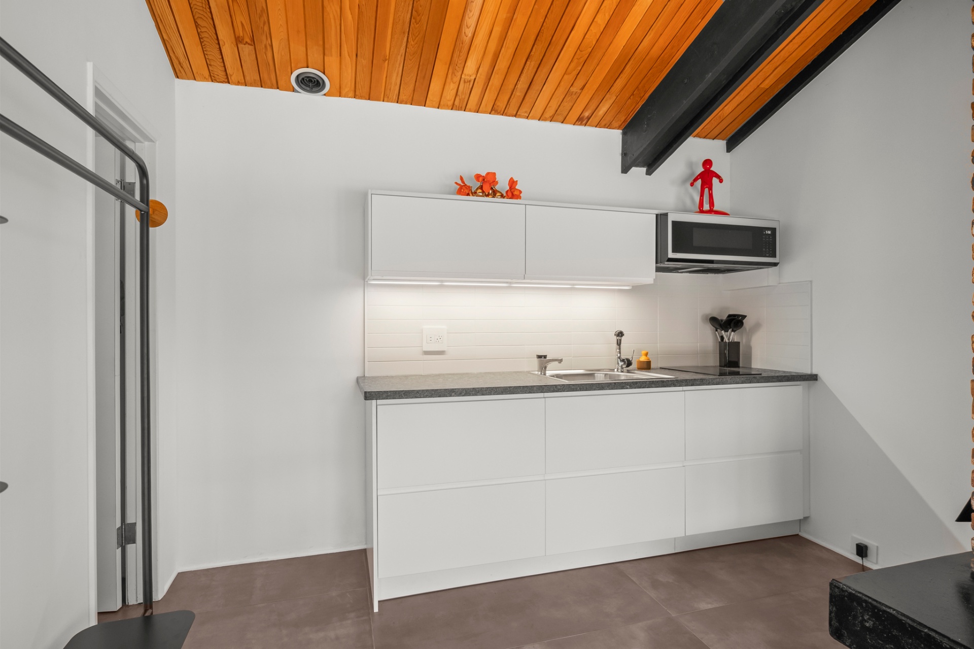 White kitchenette with stainless microwave beneath the angled wood ceiling