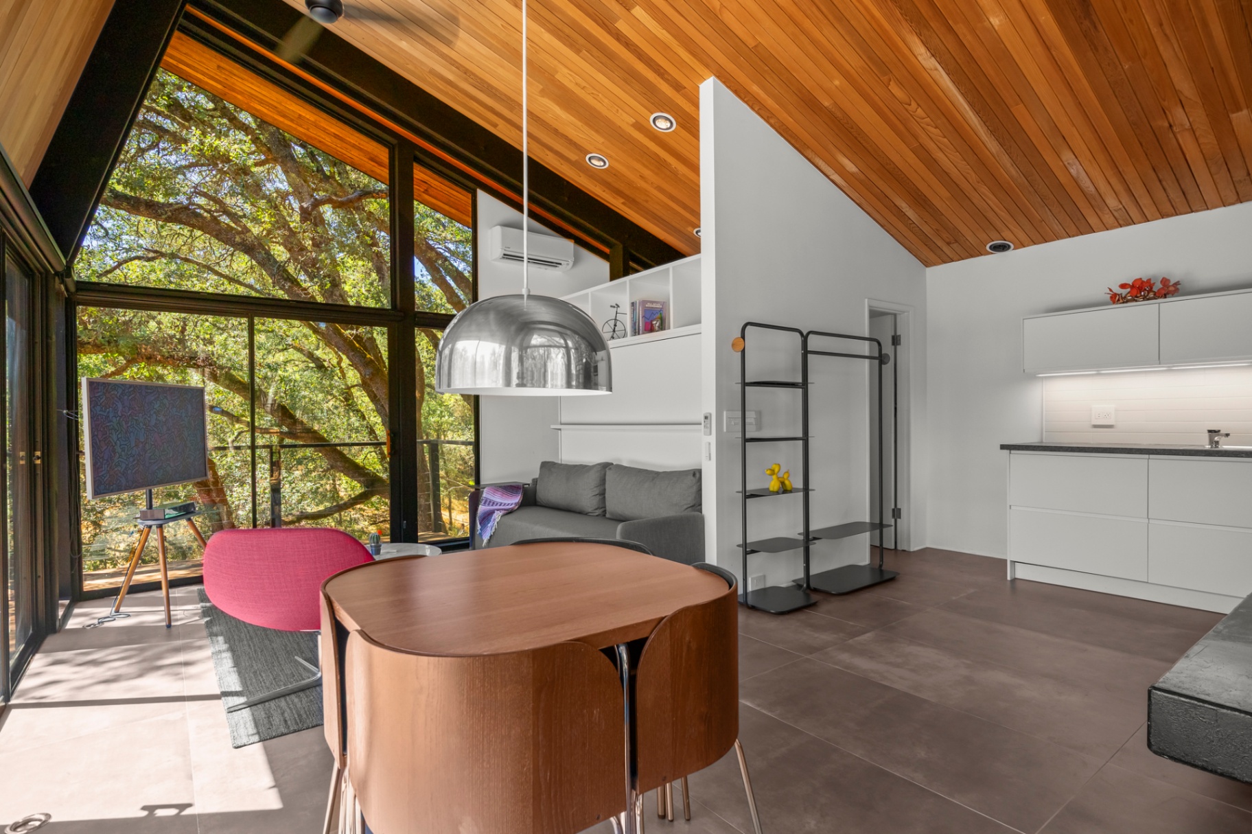 Bright open living and dining room with wood ceiling and floor-to-ceiling windows