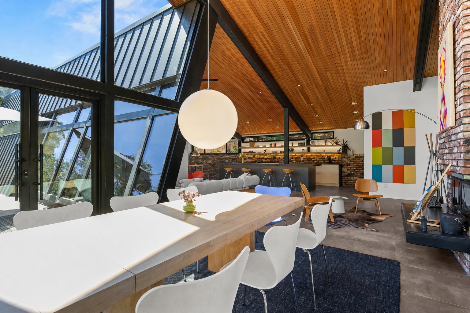 Dramatic A-frame dining room with wood ceiling, globe pendant and color-block art