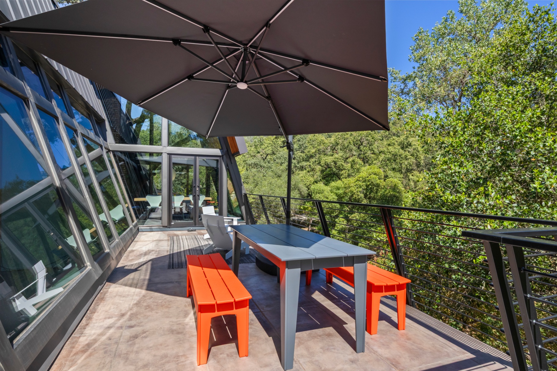 Deck dining under an umbrella with orange benches and treetop view