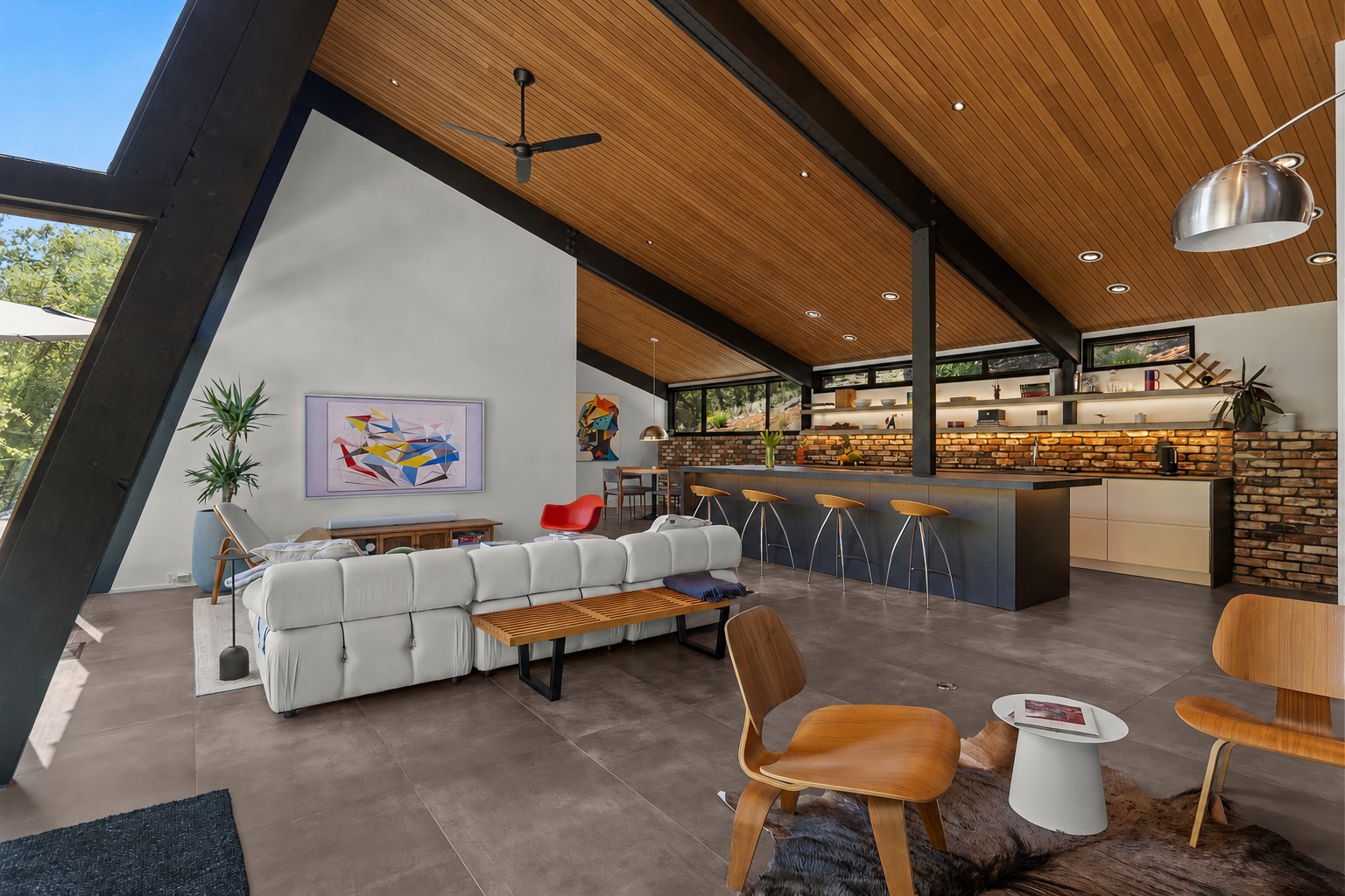 Great room full length from the fireplace, with cedar ceiling, white sectional, brick chimney and kitchen bar