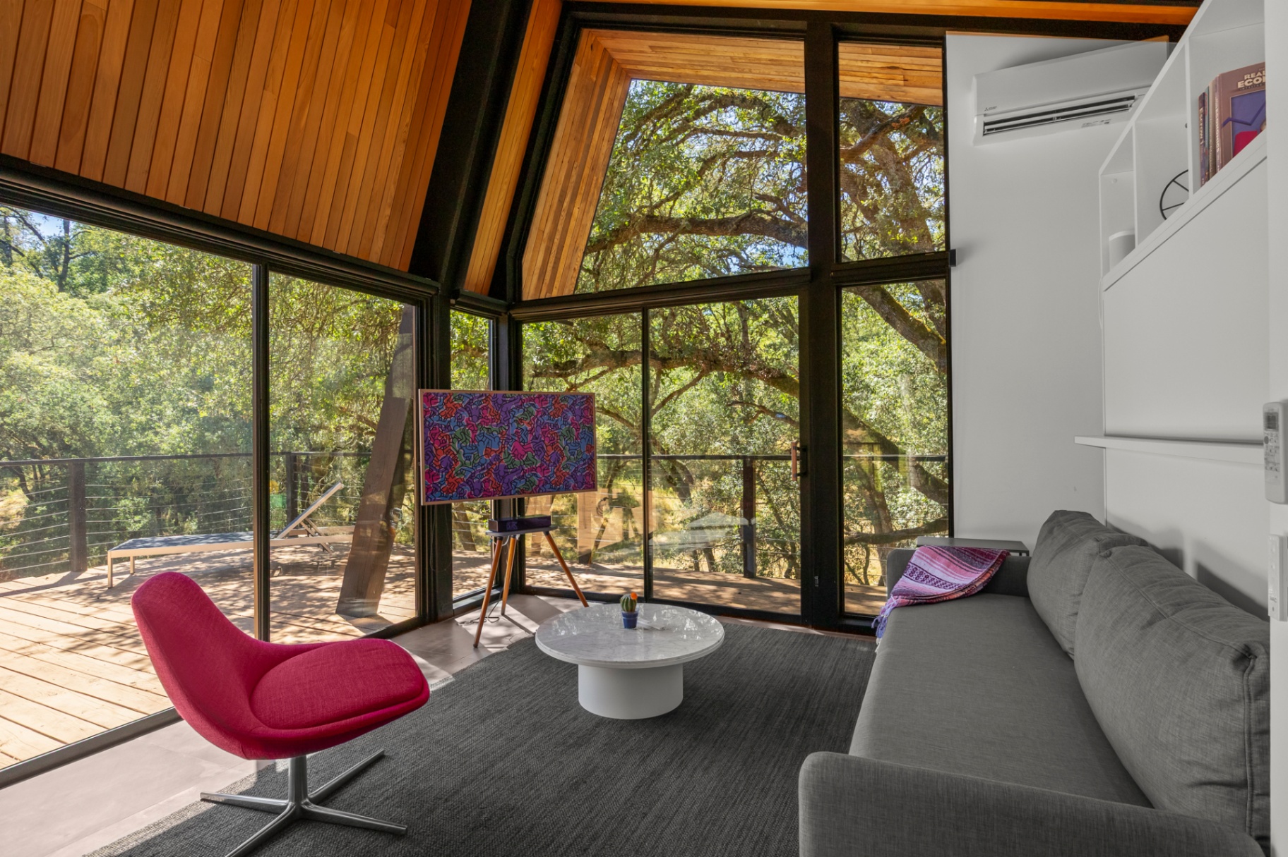 Sitting area with pink chair and wraparound windows to the trees